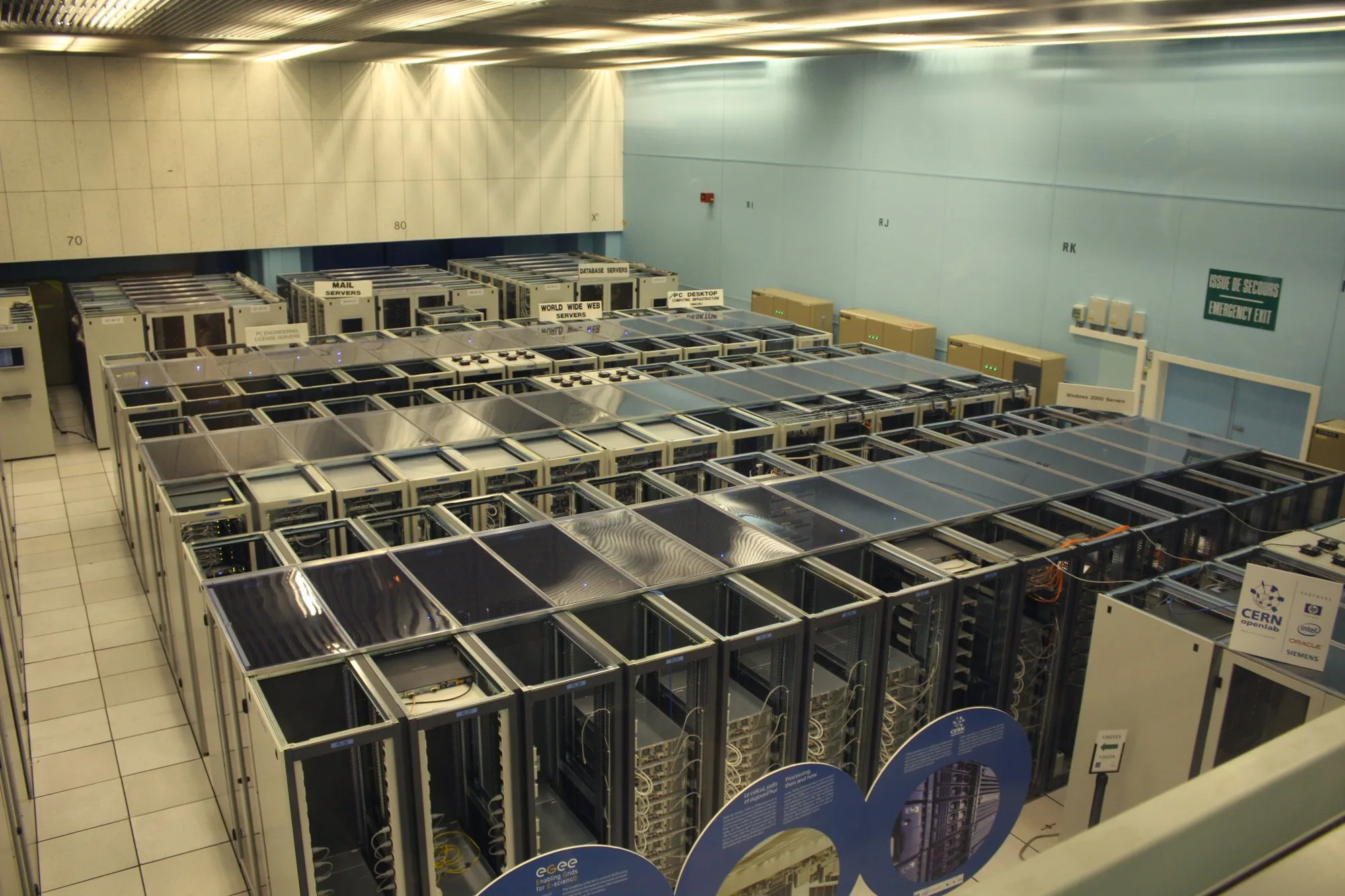 A large hall seen from above, filled with rows of tall metal racks that hold server computers (the CERN data centre in Switzerland).