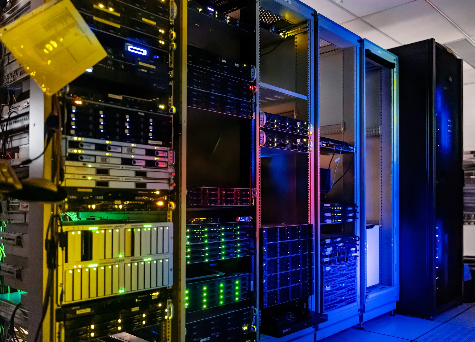Two rows of tall black server racks with small green and blue lights in a bright, cool server room.