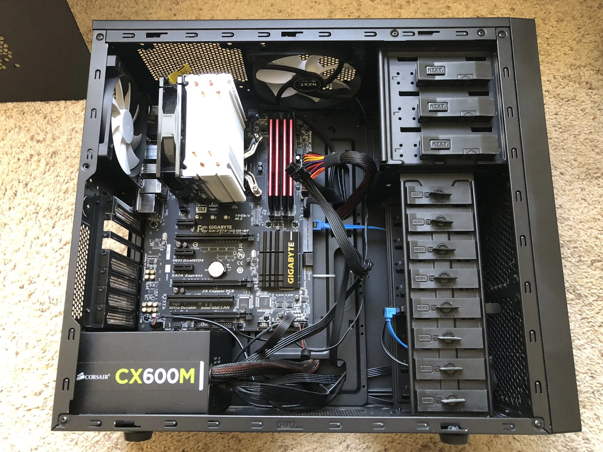 An open desktop computer case seen from above: the motherboard with a large CPU cooler, red memory sticks, cables, drive bays and a power supply labelled CX600M.