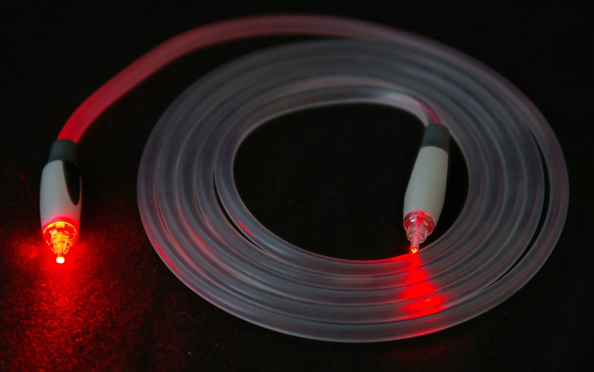 A coiled, clear fibre-optic cable on a black background; red light shines from both ends.